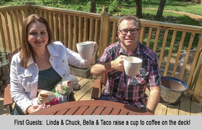 First guests, Linda and Chuck with their dogs Bella and Taco raise a cup of coffee on the deck.
